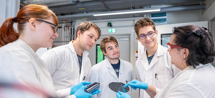 Vier Studierende und eine Lehrende in weißen Kitteln mit blauen Schutzhandschuhen
