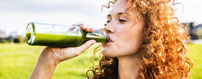 Frau mit roten Locken trinkt aus einer Glasflasche Frau mit roten Locken trinkt aus einer Glasflasche