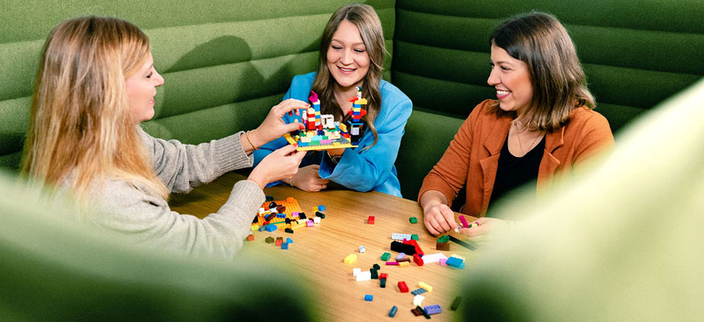 Drei junge lächelnde Personen sitzen an einem Tisch und bauen ein Modell Drei junge lächelnde Personen sitzen an einem Tisch und bauen ein Modell