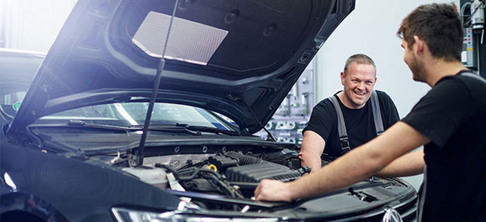 Zwei lächelnde Personen arbeiten an einem Auto mit geöffneter Motorhaube Zwei lächelnde Personen arbeiten an einem Auto mit geöffneter Motorhaube