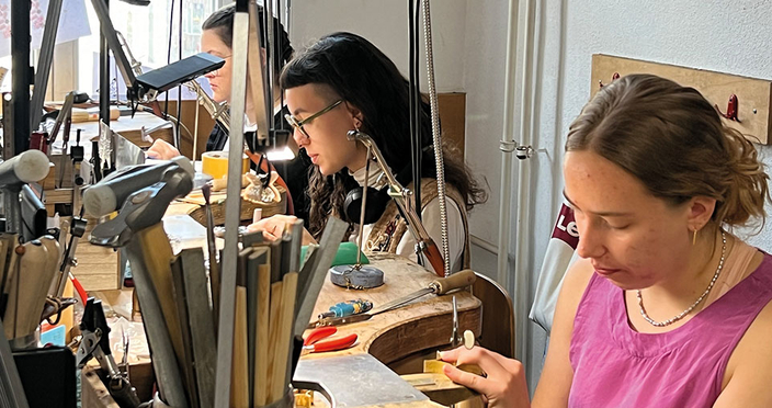 Drei junge Menschen arbeiten konzentriert an Werkbänken. Sie befinden sich in einer Werkstattumgebung mit vielen Werkzeugen und Lampen. Drei junge Menschen arbeiten konzentriert an Werkbänken. Sie befinden sich in einer Werkstattumgebung mit vielen Werkzeugen und Lampen.