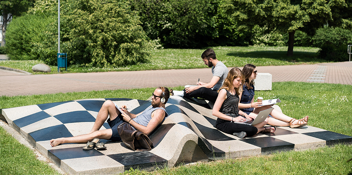 4 junge Menschen sitzen entspannt auf einer schachbrettartigen Skulpur im Park