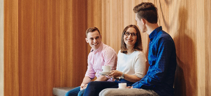 Drei gutgelaunte Mitarbeitende unterhalten sich in der Kaffepause Drei gutgelaunte Mitarbeitende unterhalten sich in der Kaffepause