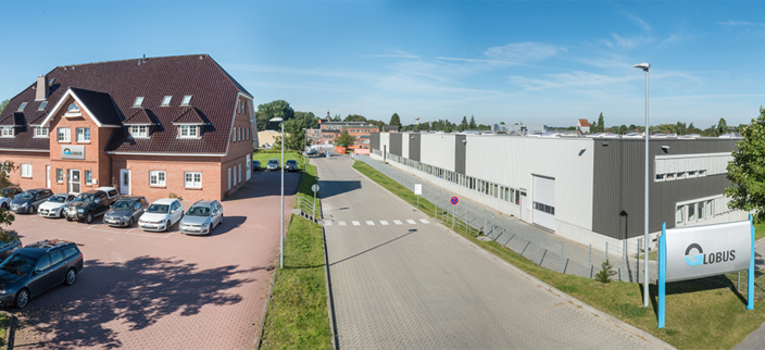 Bild einer Straße von leicht oben aufgenommen. Zu sehen ist links ein WOhnhaus und auf der rechten Seite der Straße das Firmengebäude der Globus Gummiwerke