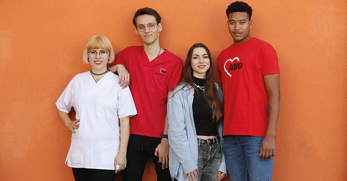 Vier Personen stehen vor einer orangen Wand und lächeln in die Kamera. Vier Personen stehen vor einer orangen Wand und lächeln in die Kamera.
