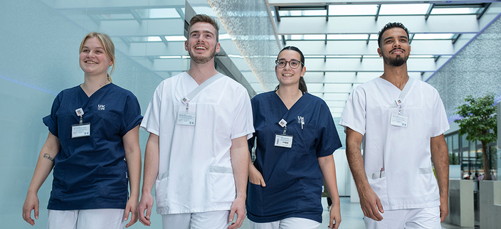 Vier Mediziner laufen durch einen Krankenhausgang mit blauen und weißen Krankenhauskleidung Vier Mediziner laufen durch einen Krankenhausgang mit blauen und weißen Krankenhauskleidung