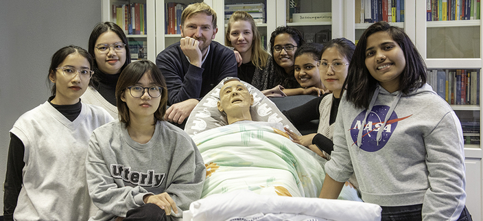 Personen um eine Pflegepuppe im Krankenbett. Personen um eine Pflegepuppe im Krankenbett.