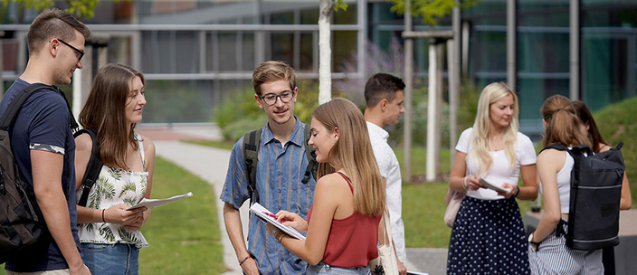 Zwei Gruppen Studierender vor einem Hochschulgebäude im lockeren Gespräch
