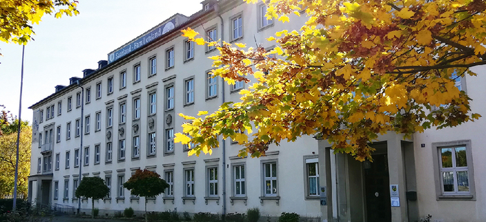 Weißes vierstöickges Gebäude mit Herbstbaum davor.