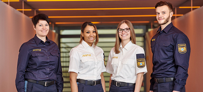 Vier Personen tragen eine Uniform, auf der "Justiz" steht und lächeln in die Kamera.
