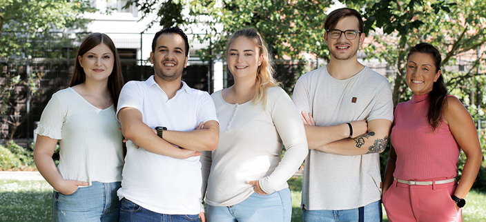 5 junge Menschen lächeln freundlich in die Kamera. Sie sind im Halbkörperporträt dargestellt und stehen bei schönem Wetter draußen eng zusammen. 5 junge Menschen lächeln freundlich in die Kamera. Sie sind im Halbkörperporträt dargestellt und stehen bei schönem Wetter draußen eng zusammen.