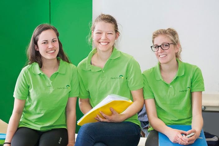 Drei junge Menschen in grünen Poloshirts mit Schullogo lächeln in die Kamera Drei junge Menschen in grünen Poloshirts mit Schullogo lächeln in die Kamera