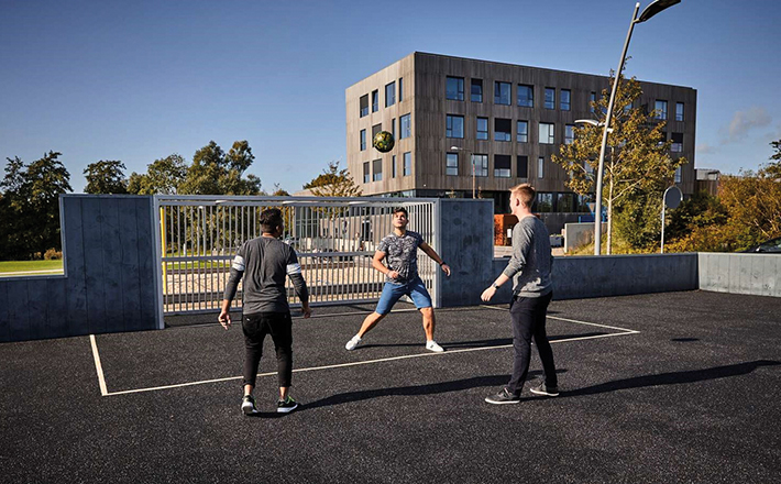 Junge ballspielende Menschen auf dem Sportplatz vor dem Universitätsgebäude
