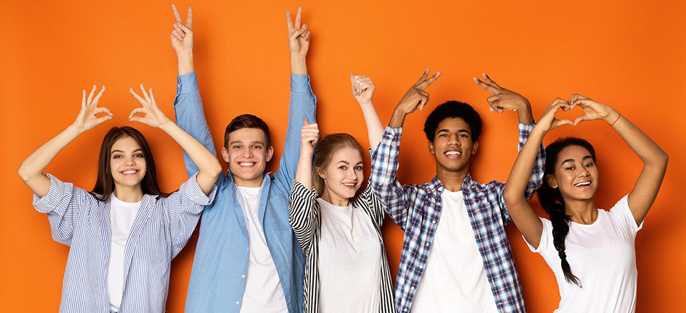 Fünf junge lächelnde Menschen vor orangefarbener Wand zeigen verschiedene Symbole mit ihren Händen