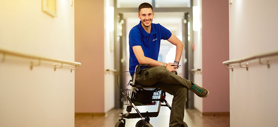 Junge lächelnde Person sitzt auf einem Rollator im Flur