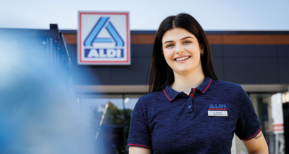 Lächelnde Auszubildende vor ALDI-Filiale