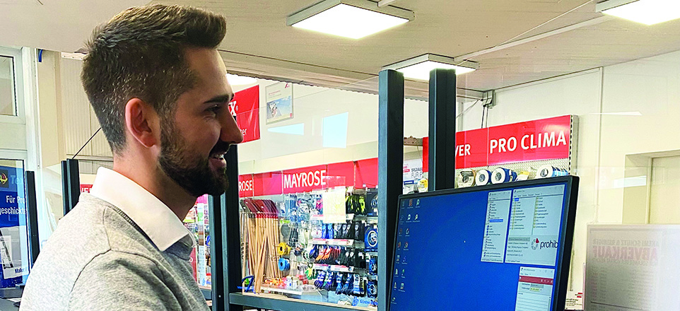 Junge lächelnde Person am Computer in der Mayrose-Filiale