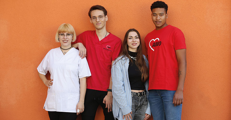 Vier Personen stehen vor einer orangen Wand und lächeln in die Kamera.
