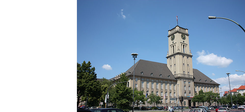 Das Bezirksamt Tempelhof-Schöneberg von Berlin mit grünen Bäumen davor bei blauem Himmel 