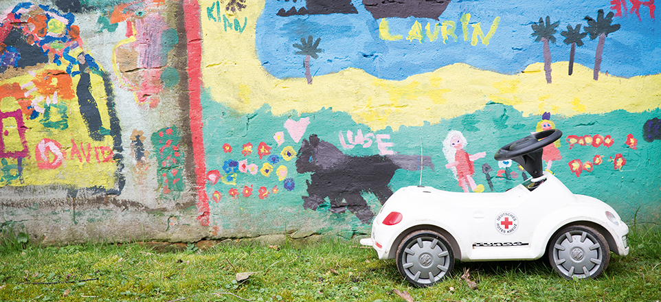 Ein weißes Bobbycar mit DRK Logo steht vor einer bunt angemalten Mauer
