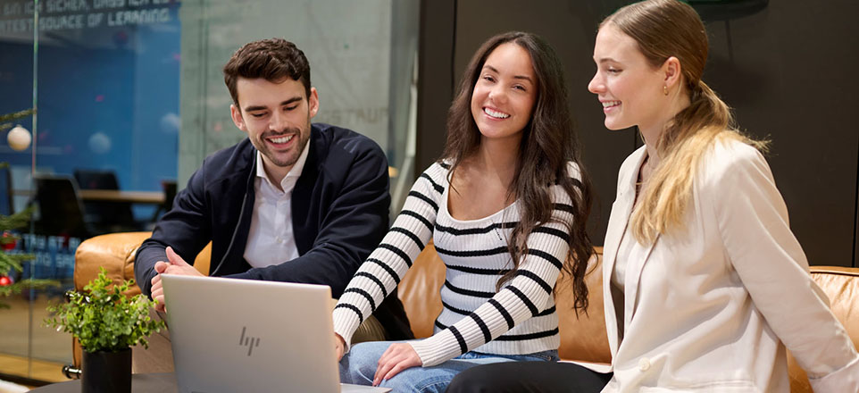 Drei junge lächelnde Personen sitzen vor einem Laptop