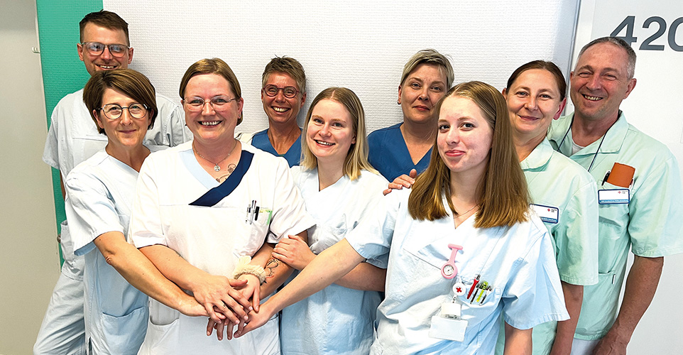 9 Pflegepersonen und Ärzte stehen zum Gruppenbild im Krankenhaus Flur