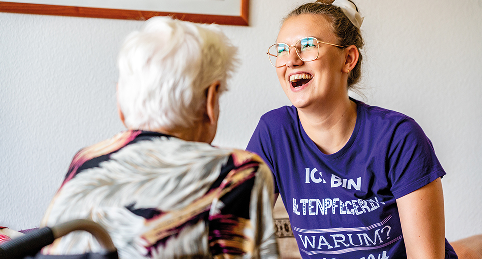 Eine Altenpflegerin lacht herzhaft im Gespräch mit einer älteren Person