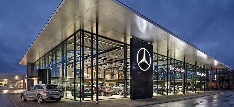 Das beleuchtete Gebäude von Klaus + Co. mit Glasfronten und großem Mercedes-Stern