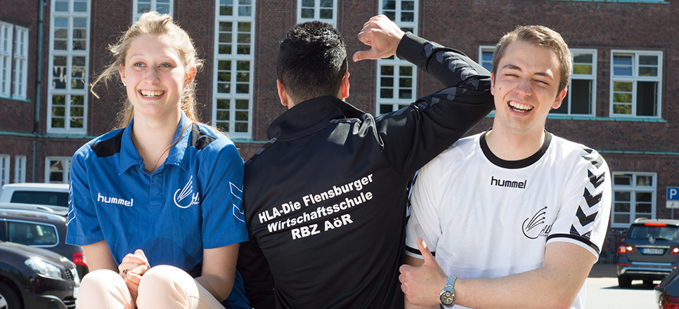 Drei lachende Jugendliche vor dem Schulgebäude