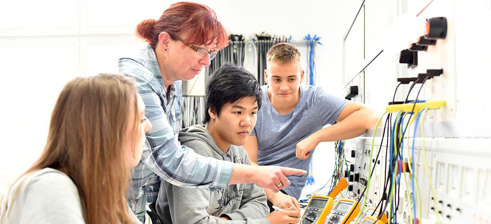 Erwachsene Person erklärt drei jungen Personen eine elektronische Anlage