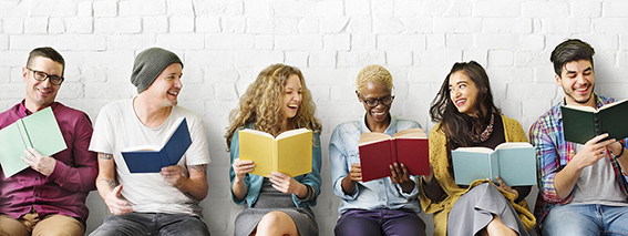 Schüler sitzen mit einem Buch in der Hand vor einer weißen Mauer