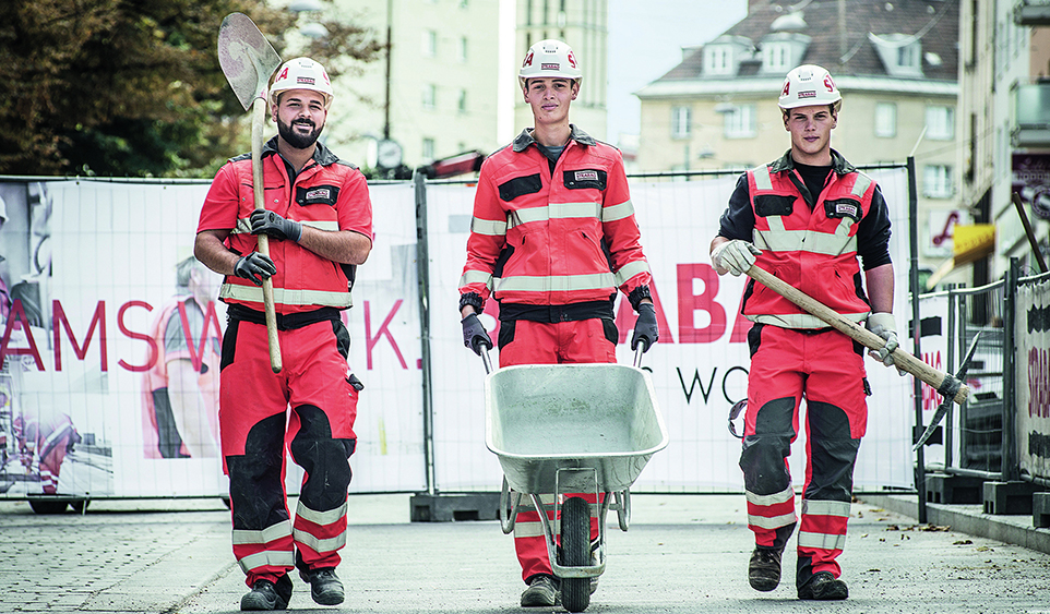 Drei junge Männer in Schutz- und Arbeitskleidung auf einer Baustelle
