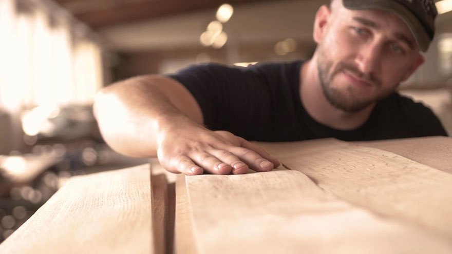 Handwerker in einer Werkstatt streicht mit der Hand über Holz. Handwerker in einer Werkstatt streicht mit der Hand über Holz.